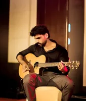Vignesh playing an acoustic guitar on stage