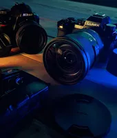 Two mirrorless cameras with lenses on a table under blue light