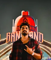 Vignesh in front of a large illuminated red sign at a night festival